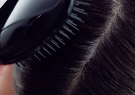 A brush strokes the crown of a woman's head distributing Garnier Express Retouch throughout her hair.